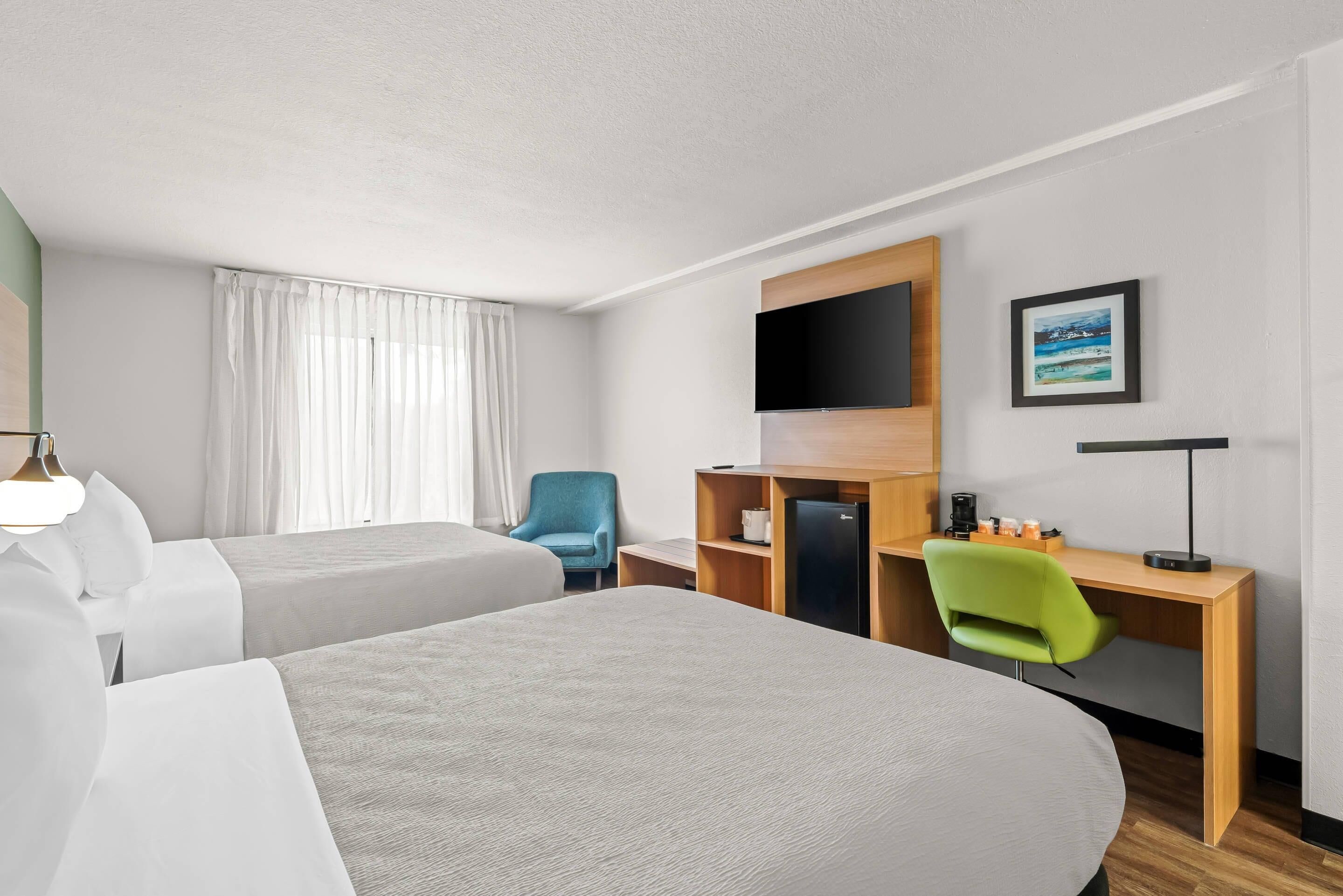 A hotel room with two beds, a desk with a computer, a TV, and a chair.