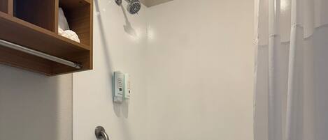 A bathroom with a white bathtub, a toilet, a shower curtain, and a wooden shelf above the toilet.