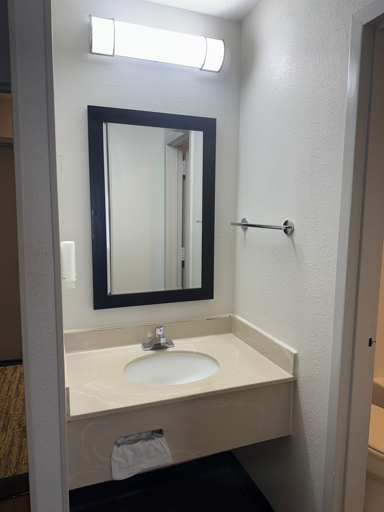 Un baño con un lavamanos blanco, un espejo y un perchero para toallas.