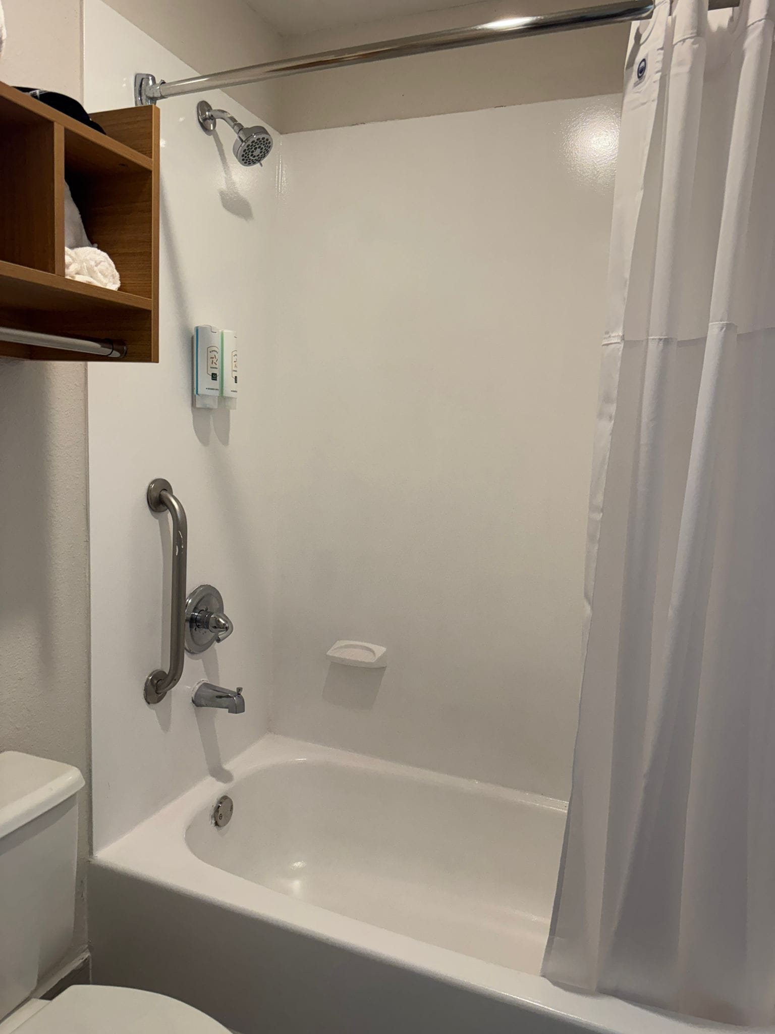 A bathroom with a white bathtub, a shower, a toilet, and a shelf with toiletries.