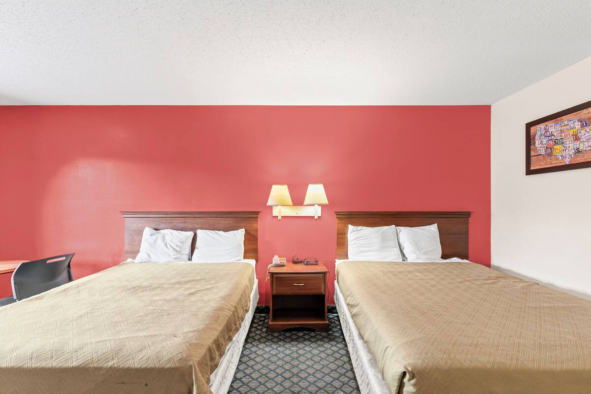Ein Hotelzimmer mit zwei Betten, einem Schreibtisch und einem Nachttisch mit Lampen.