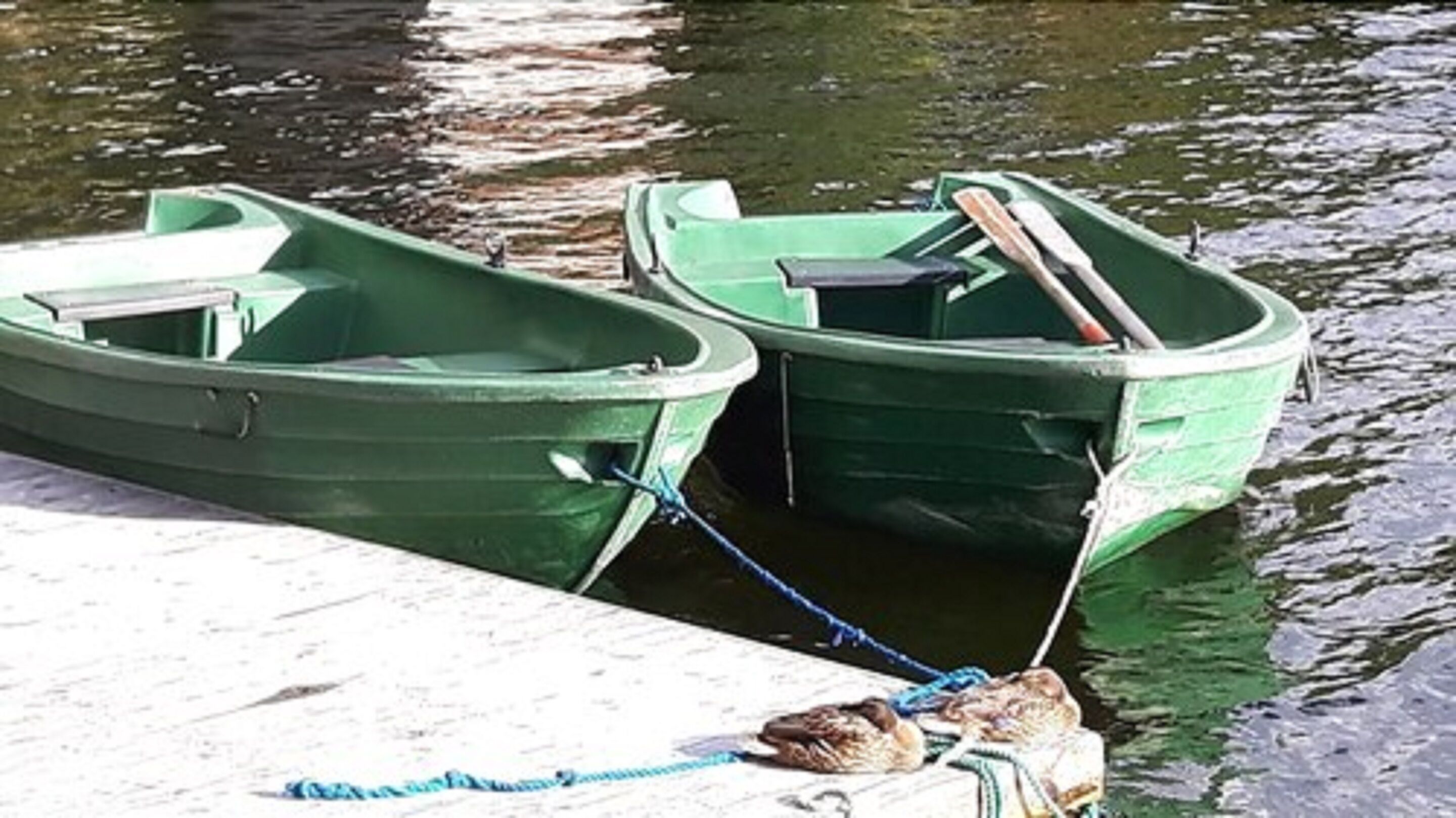 Two green boats tied to a dock.