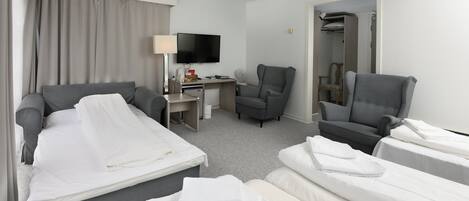 A hotel room with a bed, two armchairs, a desk with a TV, and a walk-in closet.