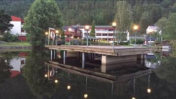 Un muelle de madera se extiende sobre un lago tranquilo, con un edificio que tiene techo rojo y fachada blanca.