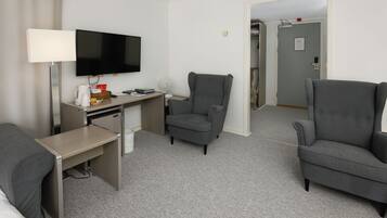 Habitación de hotel con escritorio, dos sillones, televisor y cama.