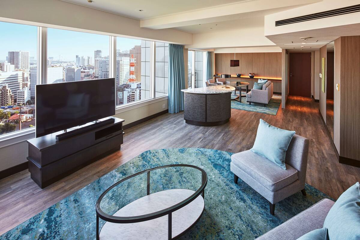 Une chambre d’hôtel moderne dotée d’une grande télévision, de sièges confortables, d’une table basse ronde et offrant une vue sur la ville.