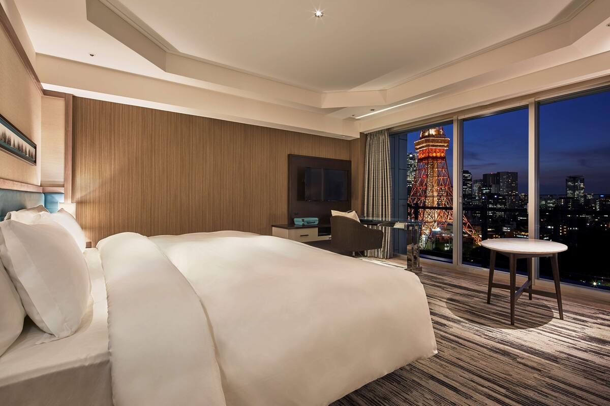 Une chambre d’hôtel moderne dotée d’un grand lit, d’un bureau et offrant une vue sur le paysage urbain et une tour illuminée la nuit.