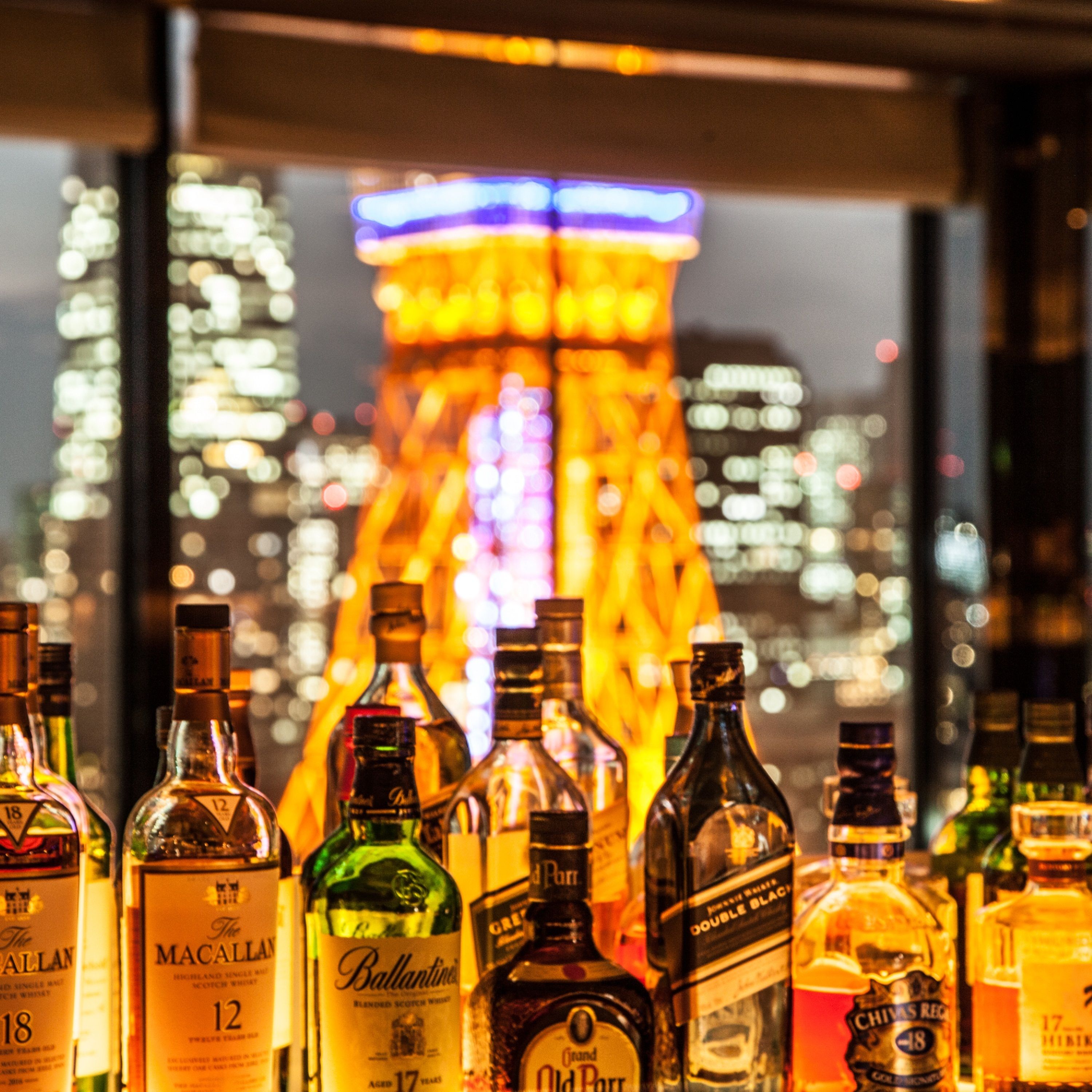 A row of liquor bottles with labels visible, set against a cityscape background with illuminated buildings.