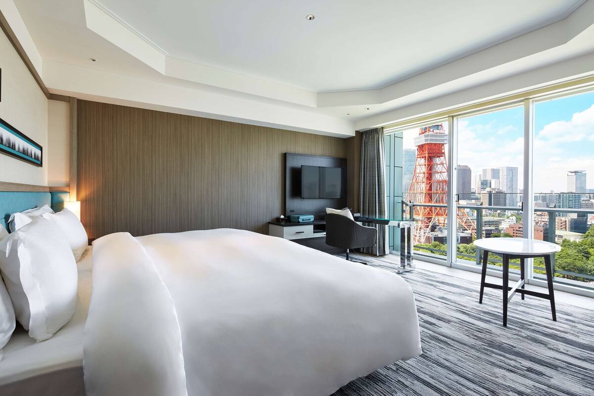 Une chambre d’hôtel avec un grand lit, un bureau avec une télévision et un balcon offrant une vue sur la ville.