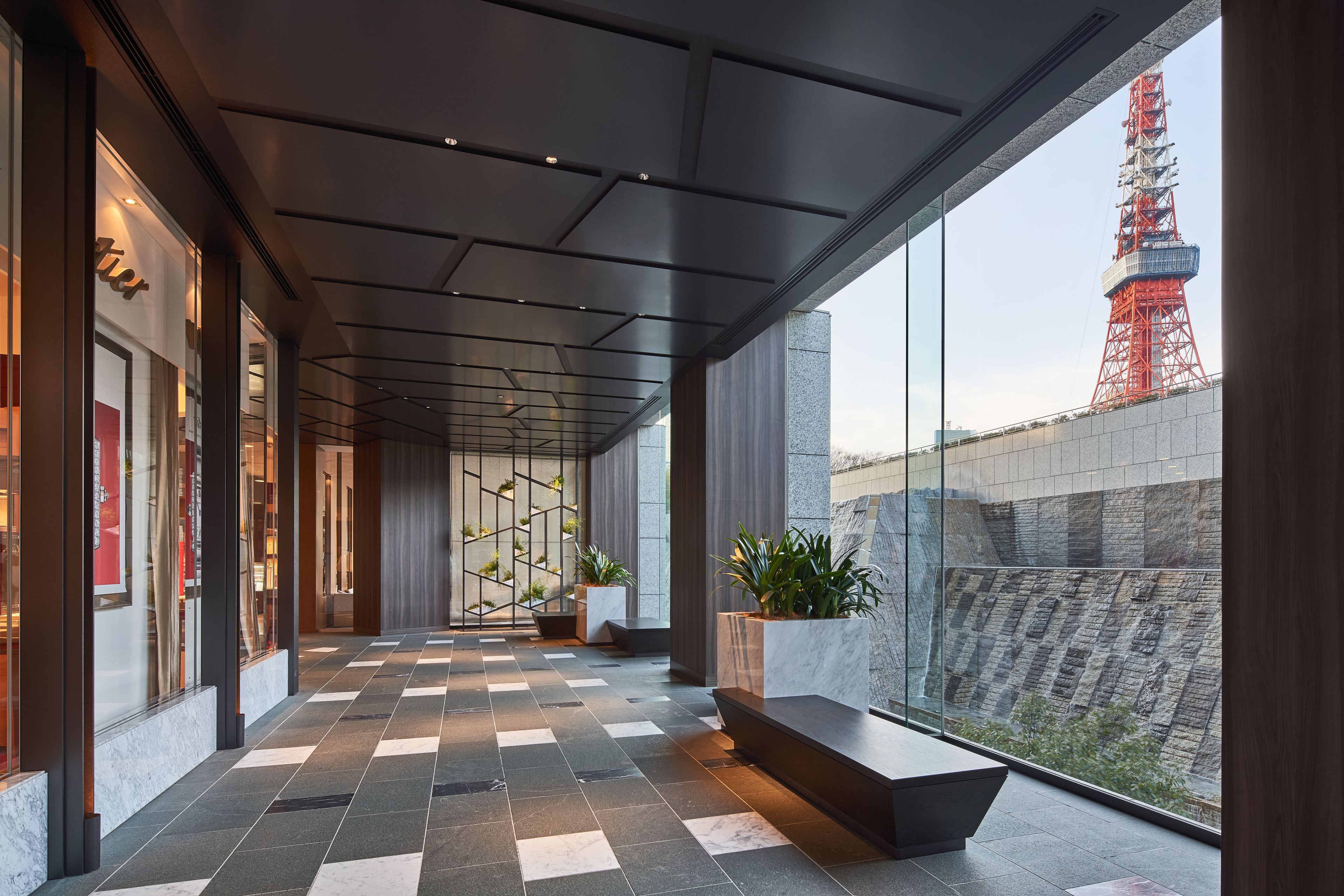 A modern hotel corridor with a checkered floor, large windows, and a view of a red tower.