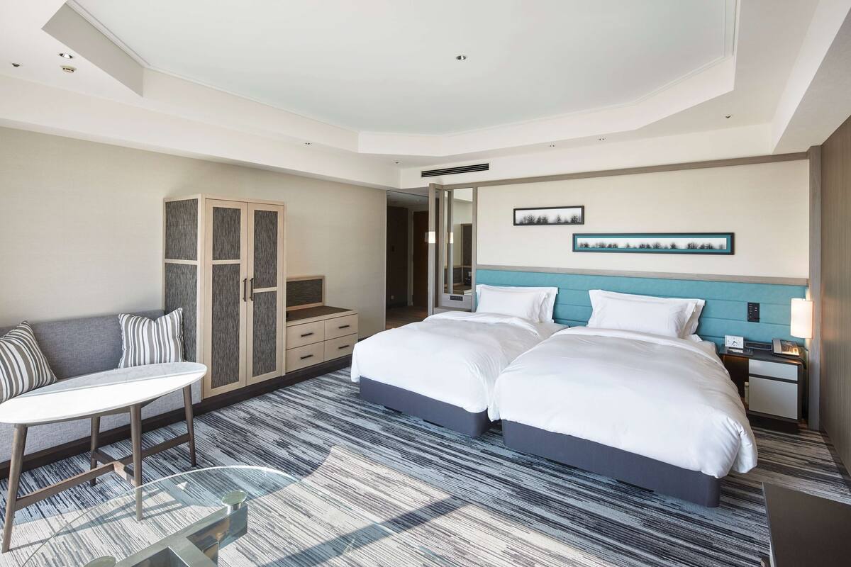 Une chambre d’hôtel moderne équipée de deux lits, d’un coin salon, d’une armoire et d’un bureau.