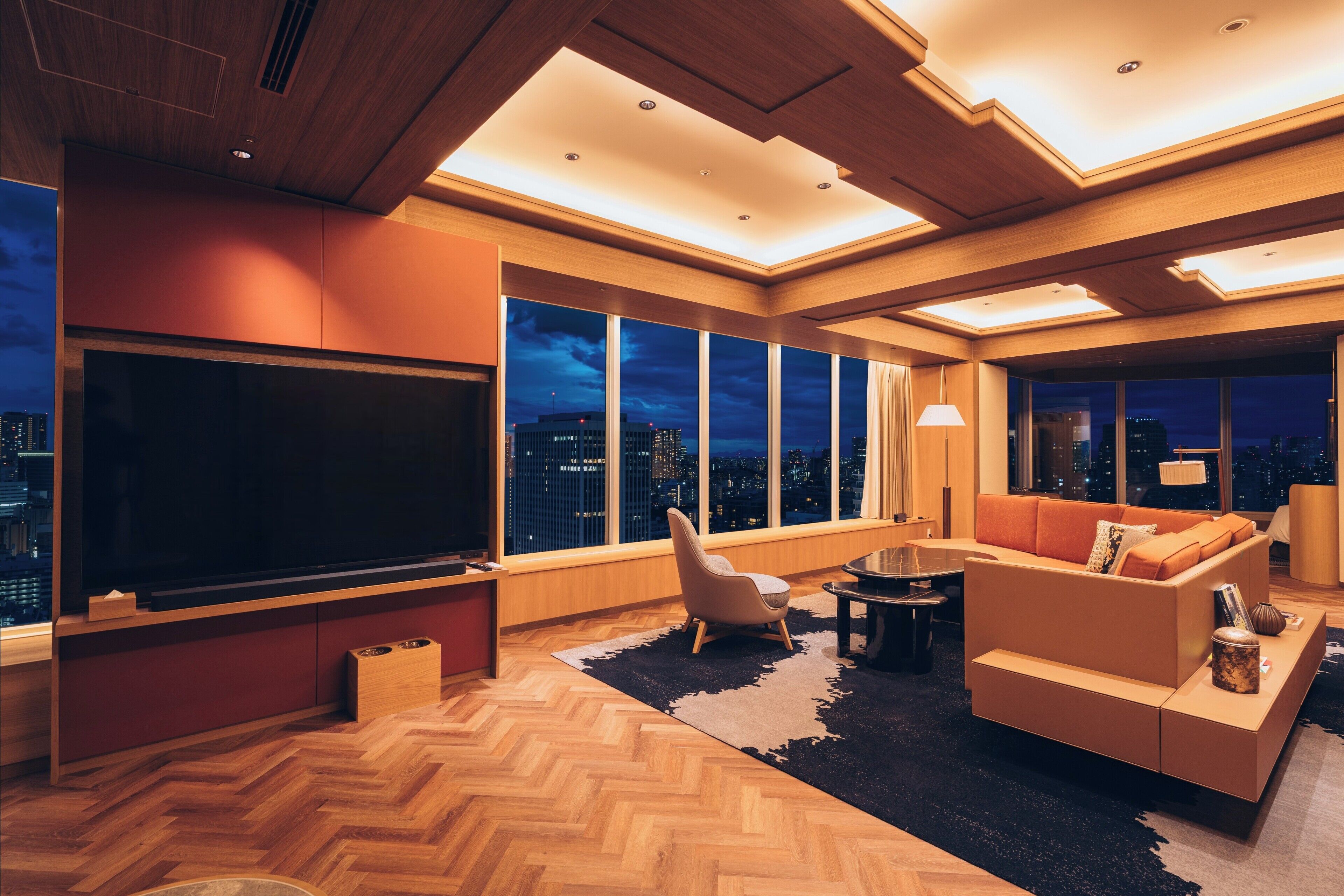 Een moderne woonkamer met een grote flatscreen televisie, comfortabele zitmogelijkheden en grote ramen met uitzicht op de stad.