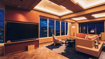 Een moderne woonkamer met een grote flatscreen televisie, comfortabele zitmogelijkheden en grote ramen met uitzicht op de stad.