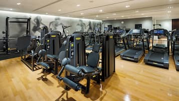 Une salle de sport équipée de divers appareils d’exercice, notamment des tapis de course et des appareils de musculation, le tout installé sur un plancher en bois.