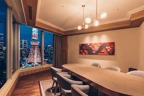 A conference room with a large table and chairs, a painting on the wall, and a view of a cityscape with a tower.