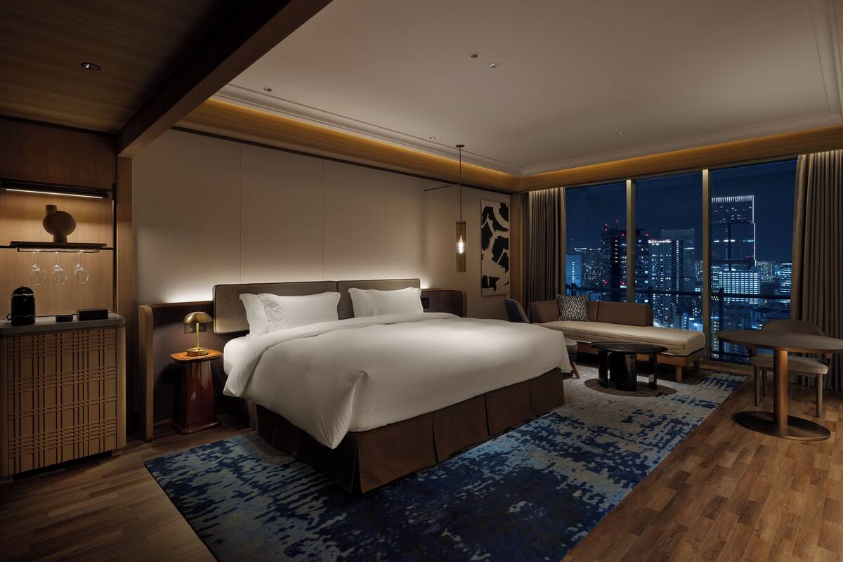 Une chambre d’hôtel moderne dotée d’un grand lit, d’un bureau, d’un canapé et offrant une vue sur le paysage urbain la nuit.
