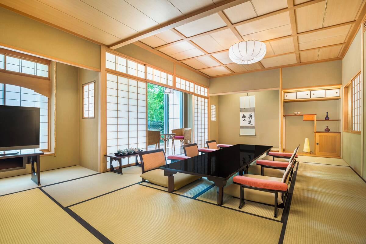 Une pièce de style japonais traditionnel, avec un sol recouvert de tatamis, une table basse avec des coussins, un téléviseur et des portes coulissantes.