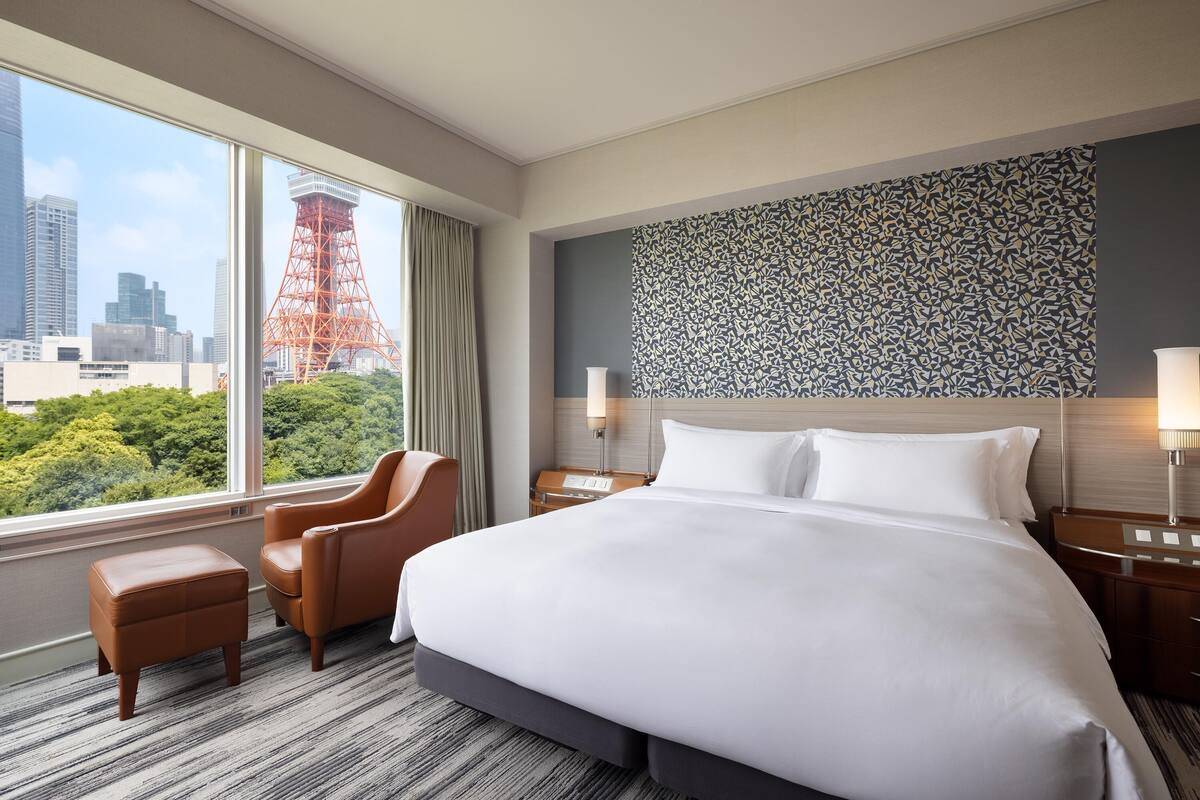 Une chambre d’hôtel avec un grand lit, une chaise, une table de chevet et une vue sur le paysage urbain, qui comprend une tour.