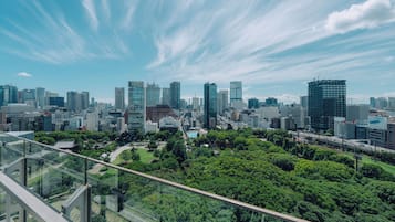 A cityscape with modern high-rise buildings, a park with dense green trees, and a clear blue sky with wispy clouds.