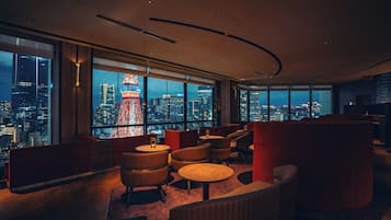 A modern lounge with large windows offering a city view, including a prominent tower.