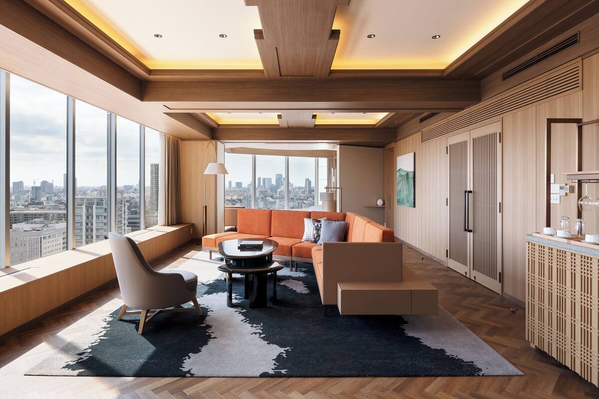 Un salon moderne avec un canapé, un fauteuil et une table basse, de grandes fenêtres offrant une vue sur la ville et des poutres apparentes en bois au plafond.
