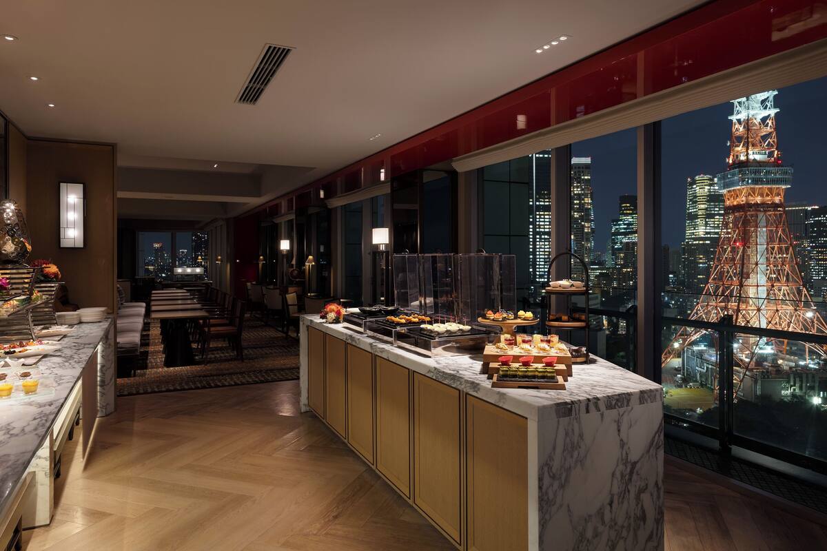 Une chambre d’hôtel moderne dotée d’un comptoir-bar en marbre pour le petit-déjeuner, offrant une vue sur la ville et agrémentée d’un mur d’accent rouge.