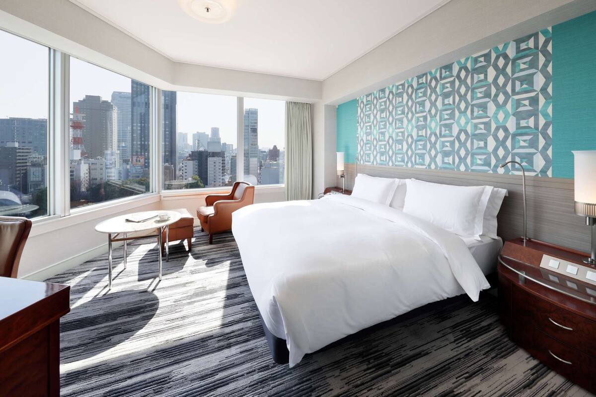 Une chambre d’hôtel avec un grand lit, un bureau, une chaise et une vue sur le paysage urbain.