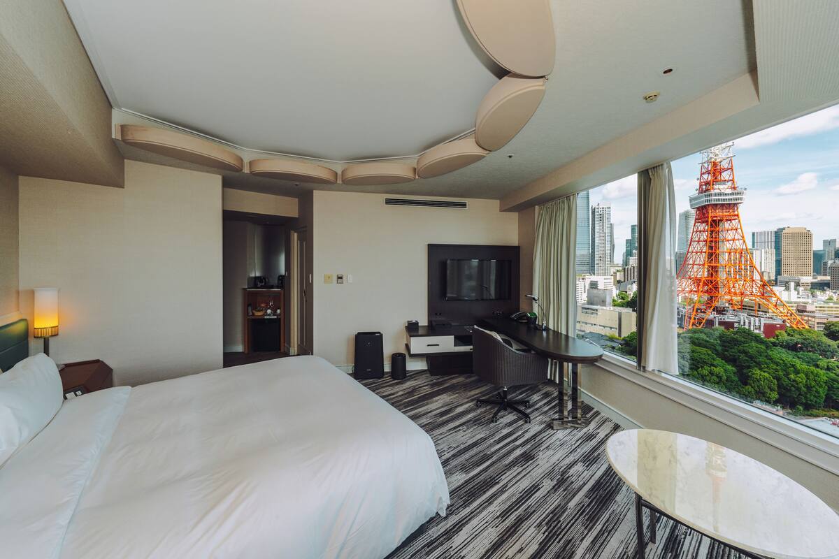 Une chambre d’hôtel avec un grand lit, un bureau, une chaise, une télévision et une vue sur le paysage urbain, avec une tour en particulier.