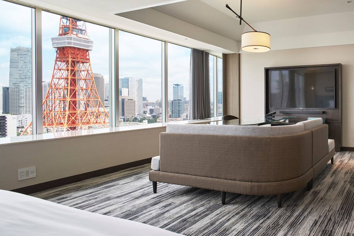 Une chambre d’hôtel avec une grande fenêtre, un canapé, une télévision et une vue sur la ville.