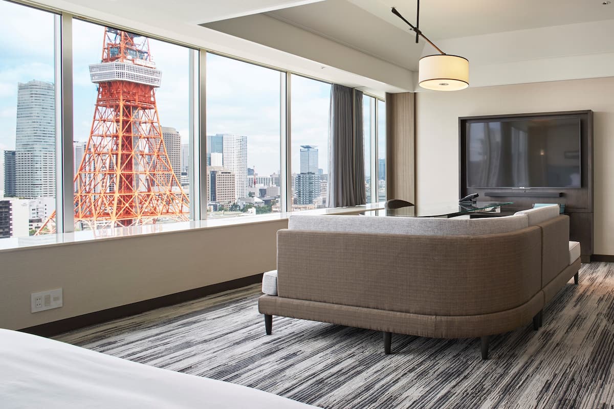 Enjoy a panoramic city view from the large window, featuring a prominent tower. The room offers a comfortable sofa, flat-screen TV, and modern light fixture.