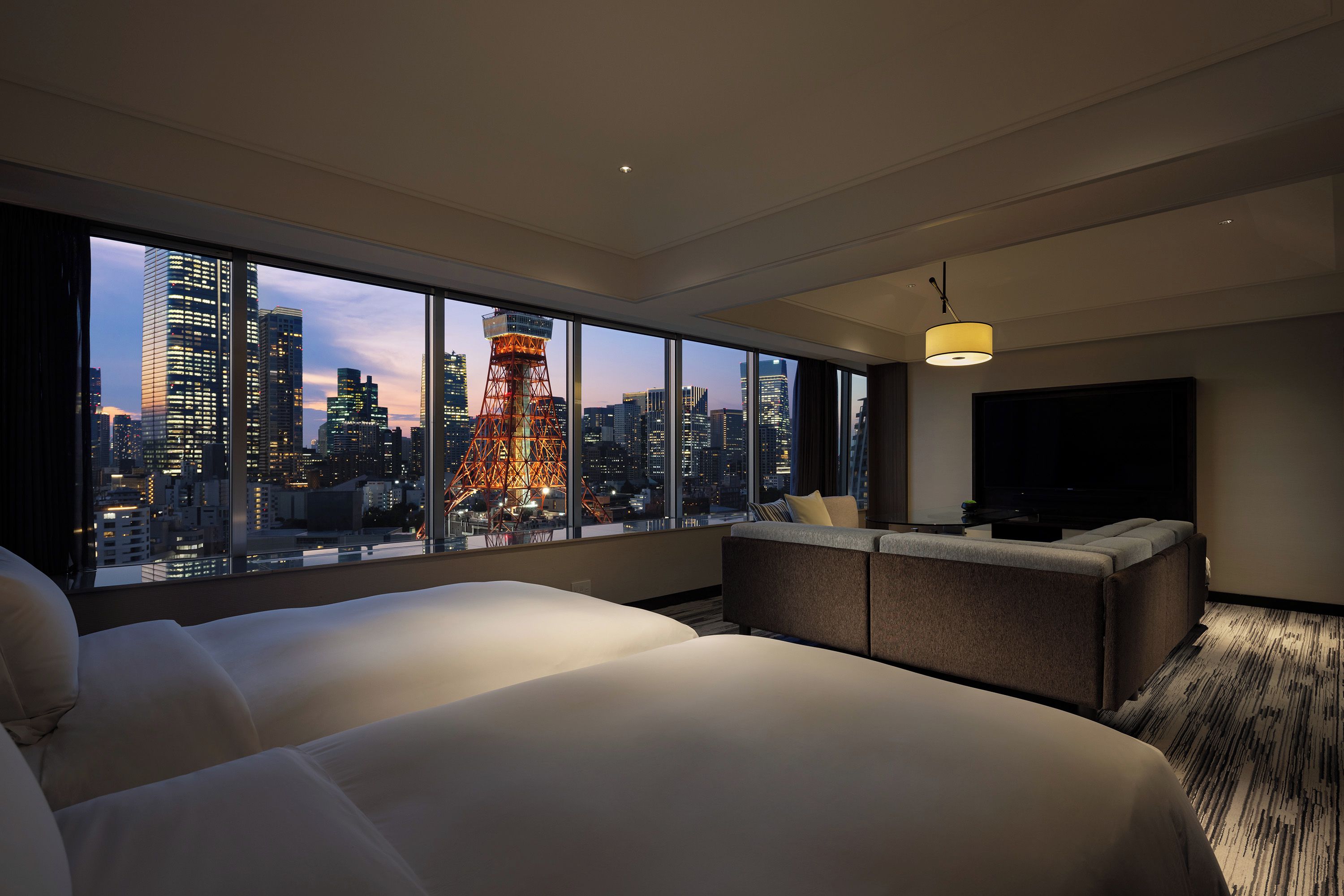 A hotel room with a large window, a bed, a seating area, and a flat-screen TV.