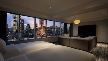 A hotel room with a large window, a bed, a seating area, and a flat-screen TV.