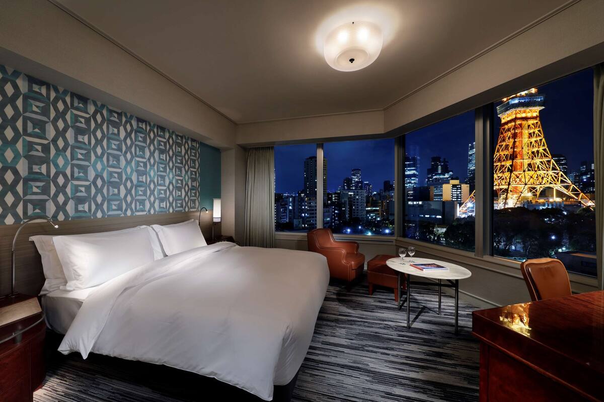Une chambre d’hôtel avec un grand lit, un bureau, une chaise et une vue sur la Tour Eiffel la nuit.