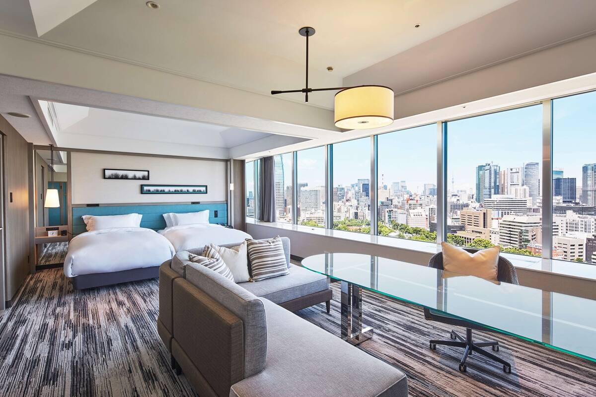 Une chambre d’hôtel moderne avec un grand lit, un canapé, une table en verre et une vue sur la ville.