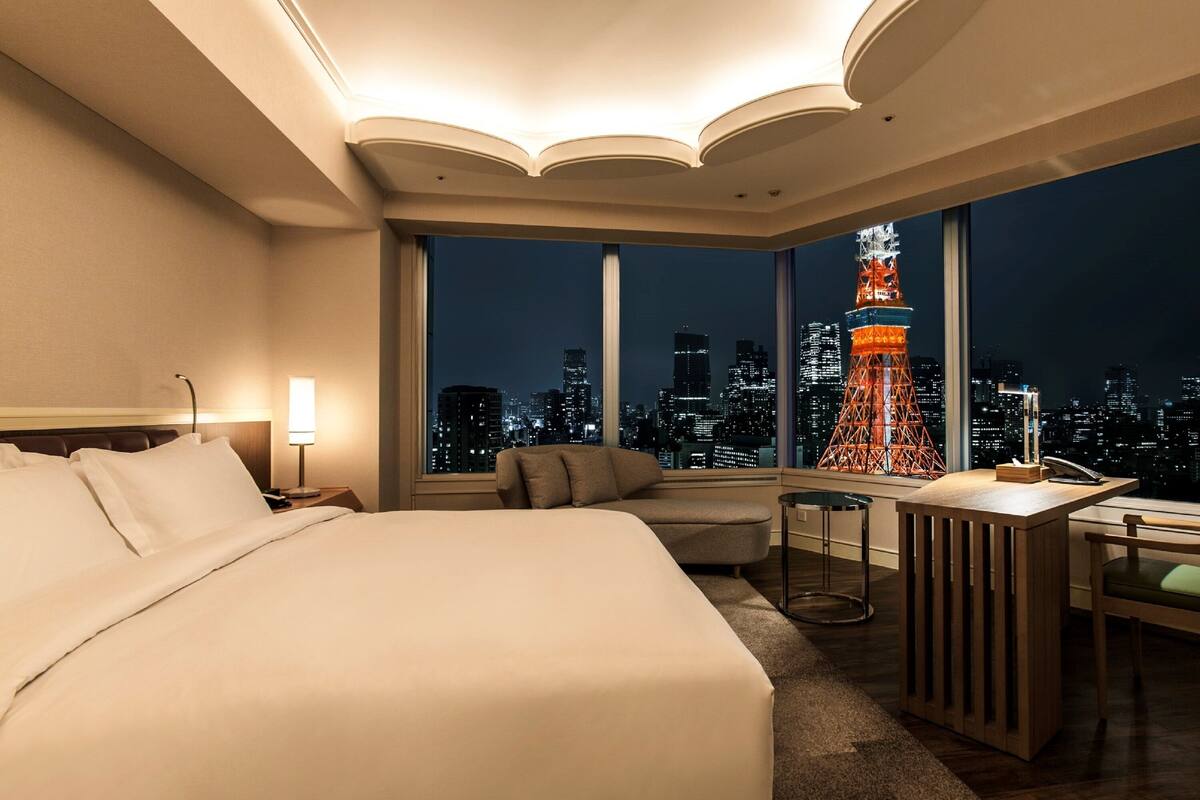 Une chambre d’hôtel avec un grand lit, un bureau, une chaise et une vue sur le paysage urbain et un monument illuminé la nuit.