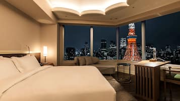 Une chambre d’hôtel avec un grand lit, un bureau, une chaise et une vue sur le paysage urbain et un monument illuminé la nuit.