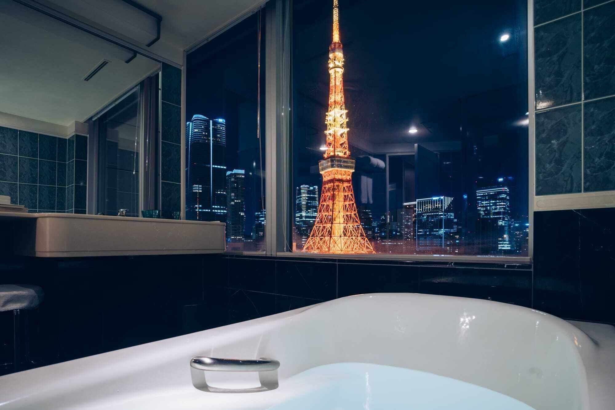 A bathroom with a bathtub, a window with a view of the Eiffel Tower at night, and a cityscape.