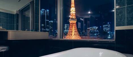 A bathroom with a bathtub, a window with a view of the Eiffel Tower at night, and a cityscape.