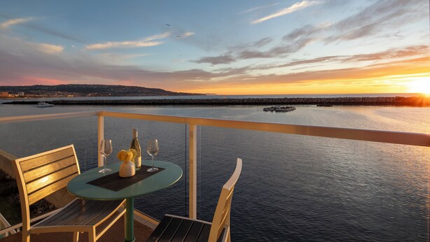 Mesa com garrafa e copos, com vista para um corpo de água ao pôr do sol.