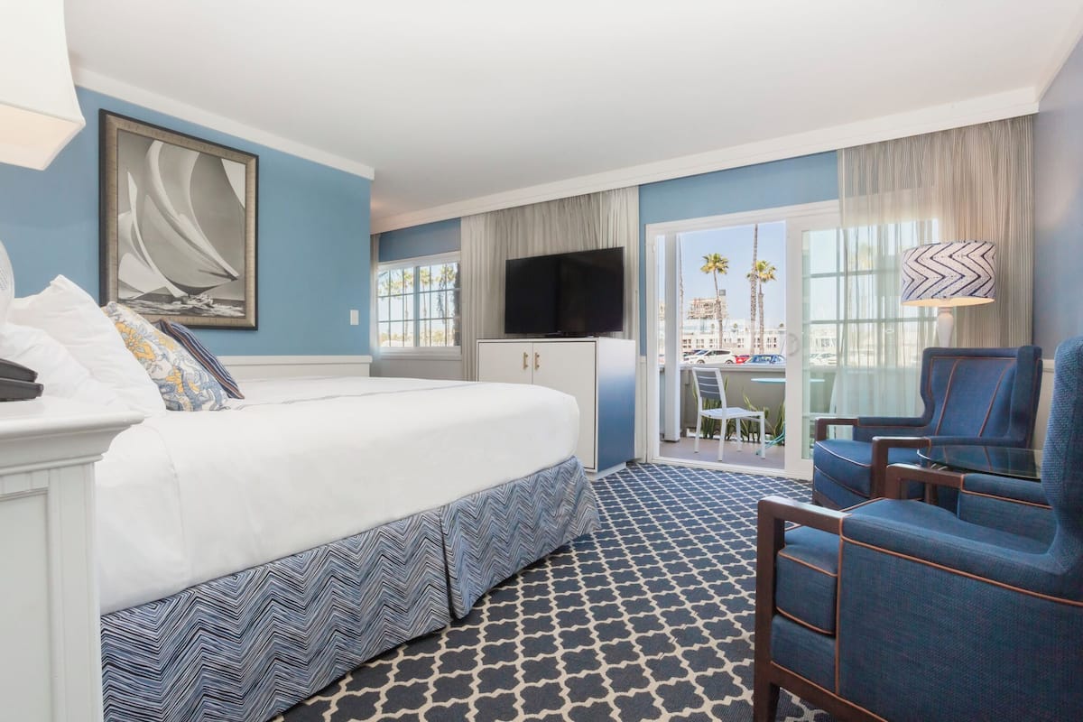 A hotel room with a bed, a TV, a seating area with chairs, a desk, and a view of palm trees.