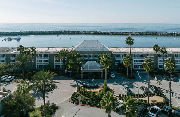 A hotel with a central glass atrium, parking lot, and a view of the ocean.