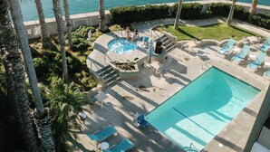 Uma área de piscina com espreguiçadeiras e uma piscina pequena, rodeada por palmeiras e vista para o mar.