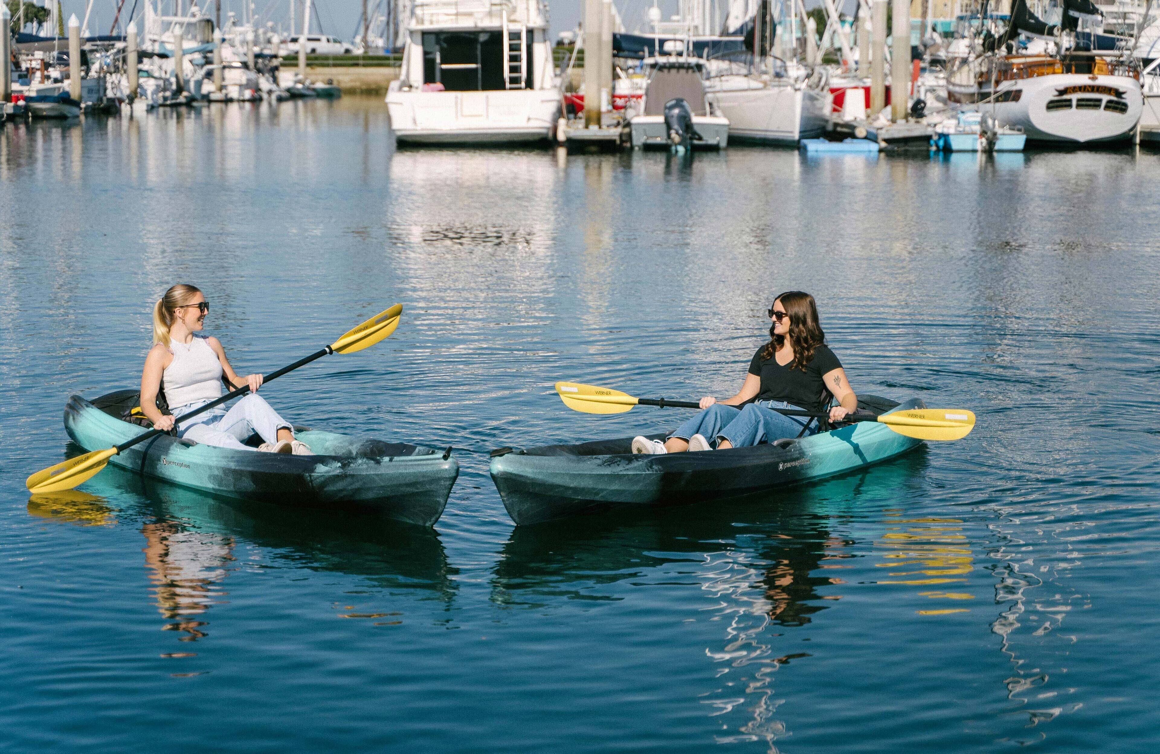 Dos personas hacen kayak en aguas tranquilas, con un puerto deportivo al fondo.