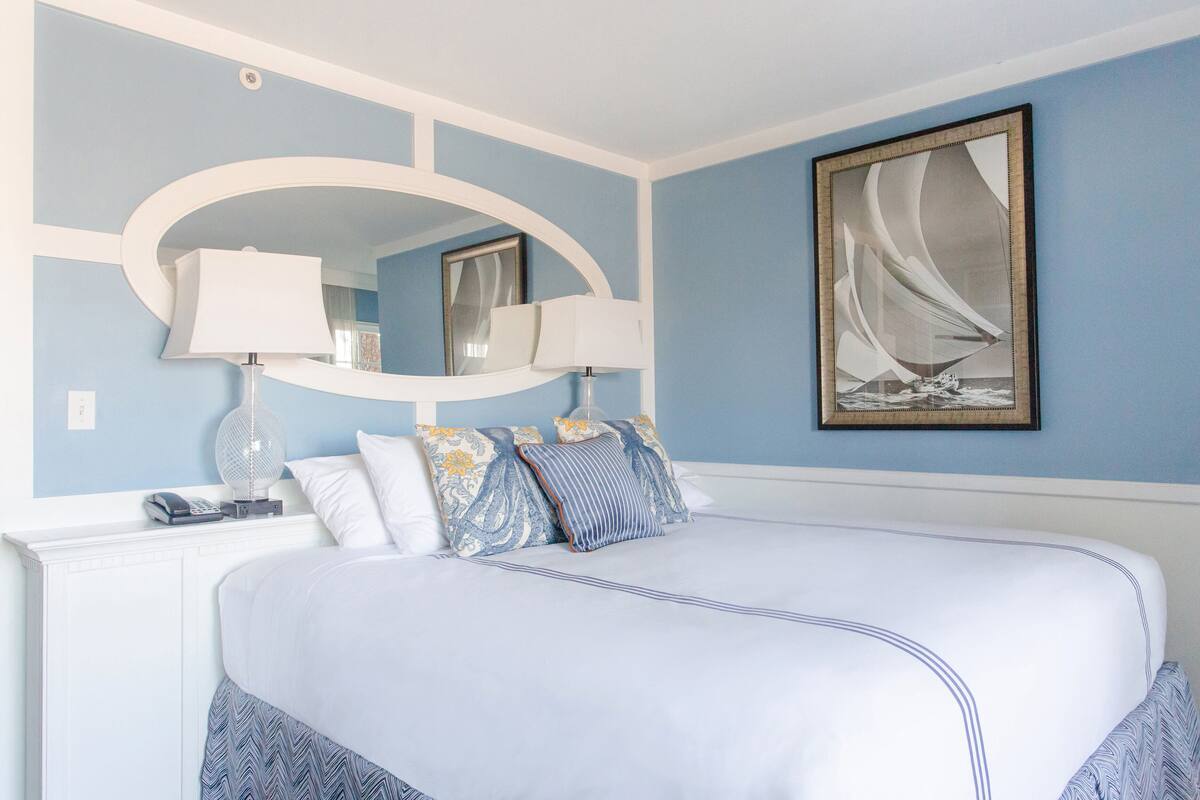 A bedroom with a large bed, two bedside lamps, a mirror, and a framed picture on the wall.