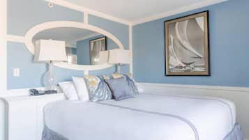 A bedroom with a large bed, two bedside lamps, a mirror, and a framed picture on the wall.