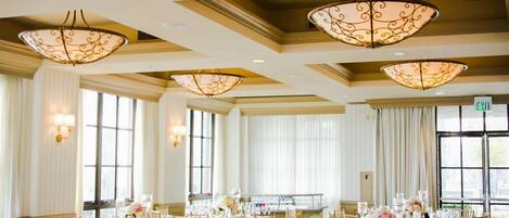 Un salón de banquetes con mesas redondas, sillas doradas y grandes candelabros.