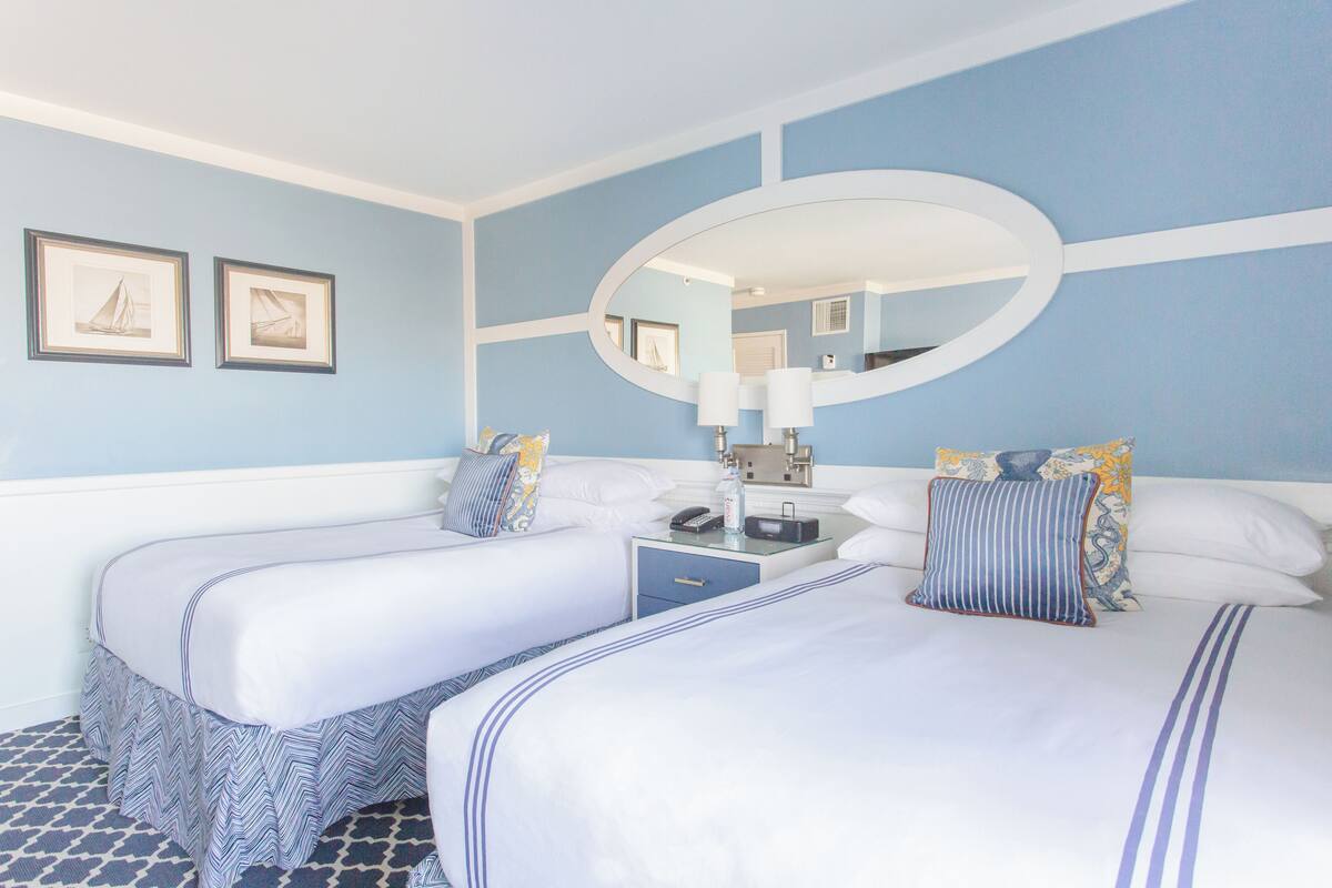 A hotel room with two beds, a large mirror, and a nightstand with a lamp.