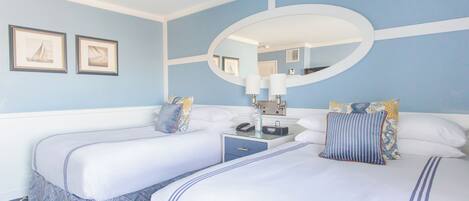 A hotel room with two beds, a large mirror, and a nightstand with a lamp.