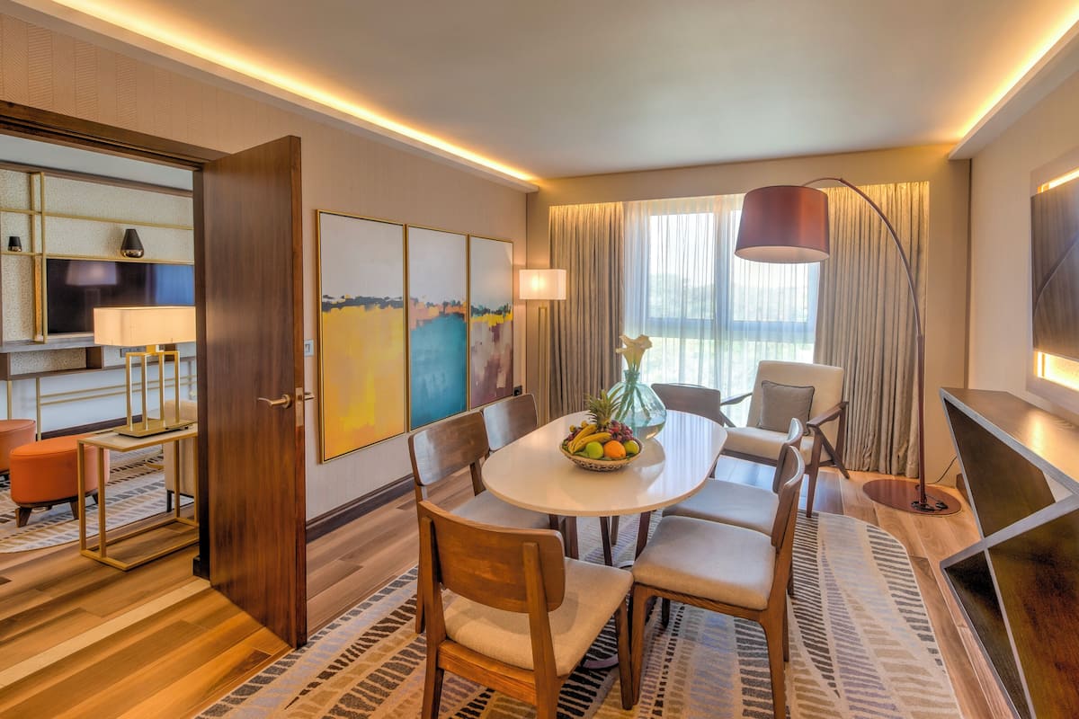 A hotel room with a dining area, a sofa, a TV, and a large window with curtains.