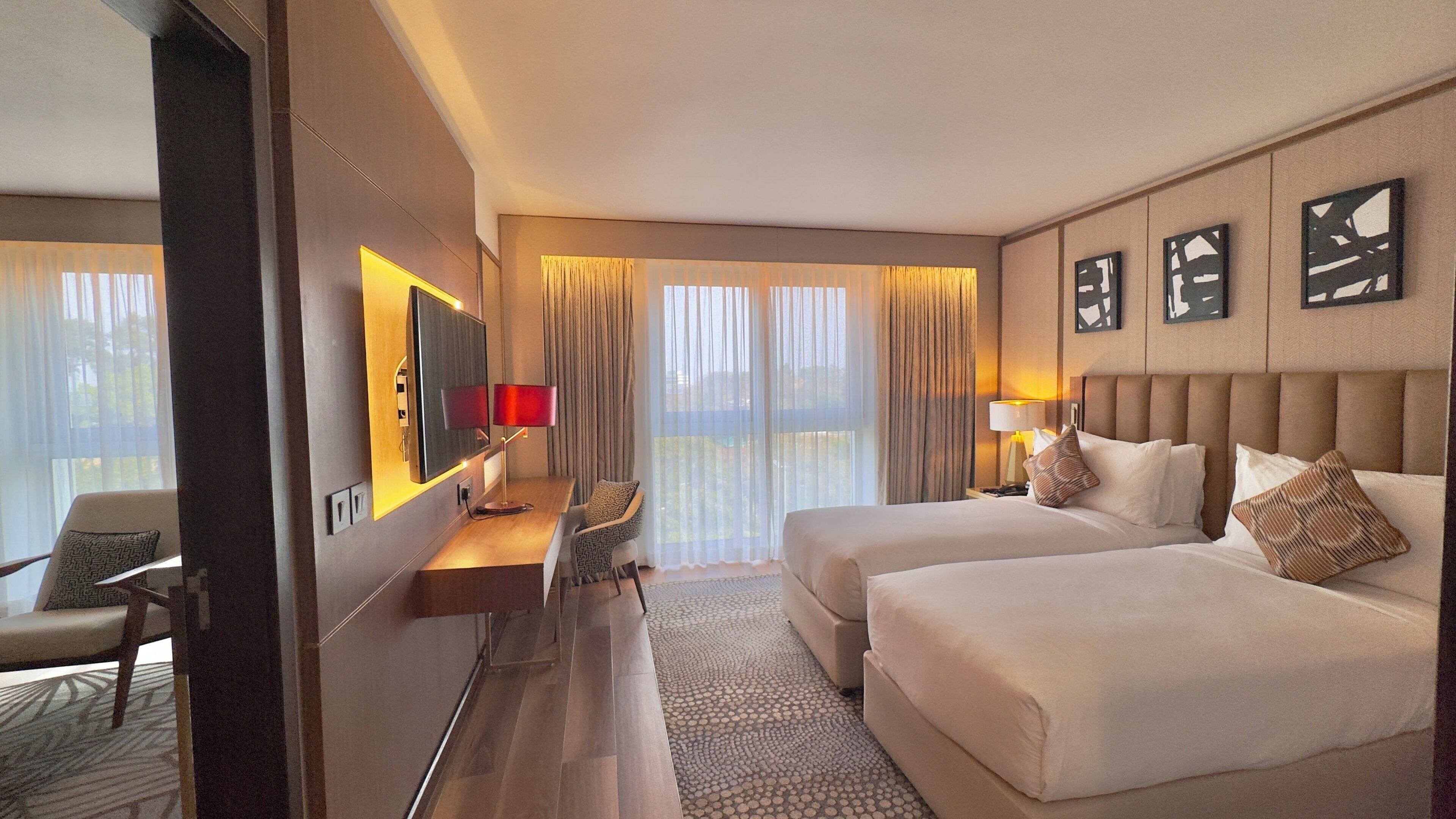 A hotel room with a bed, a desk, a chair, a TV, and a window with curtains.